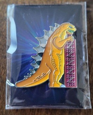 Yellow Godzilla enamel pin on starburst backing card in protective plastic